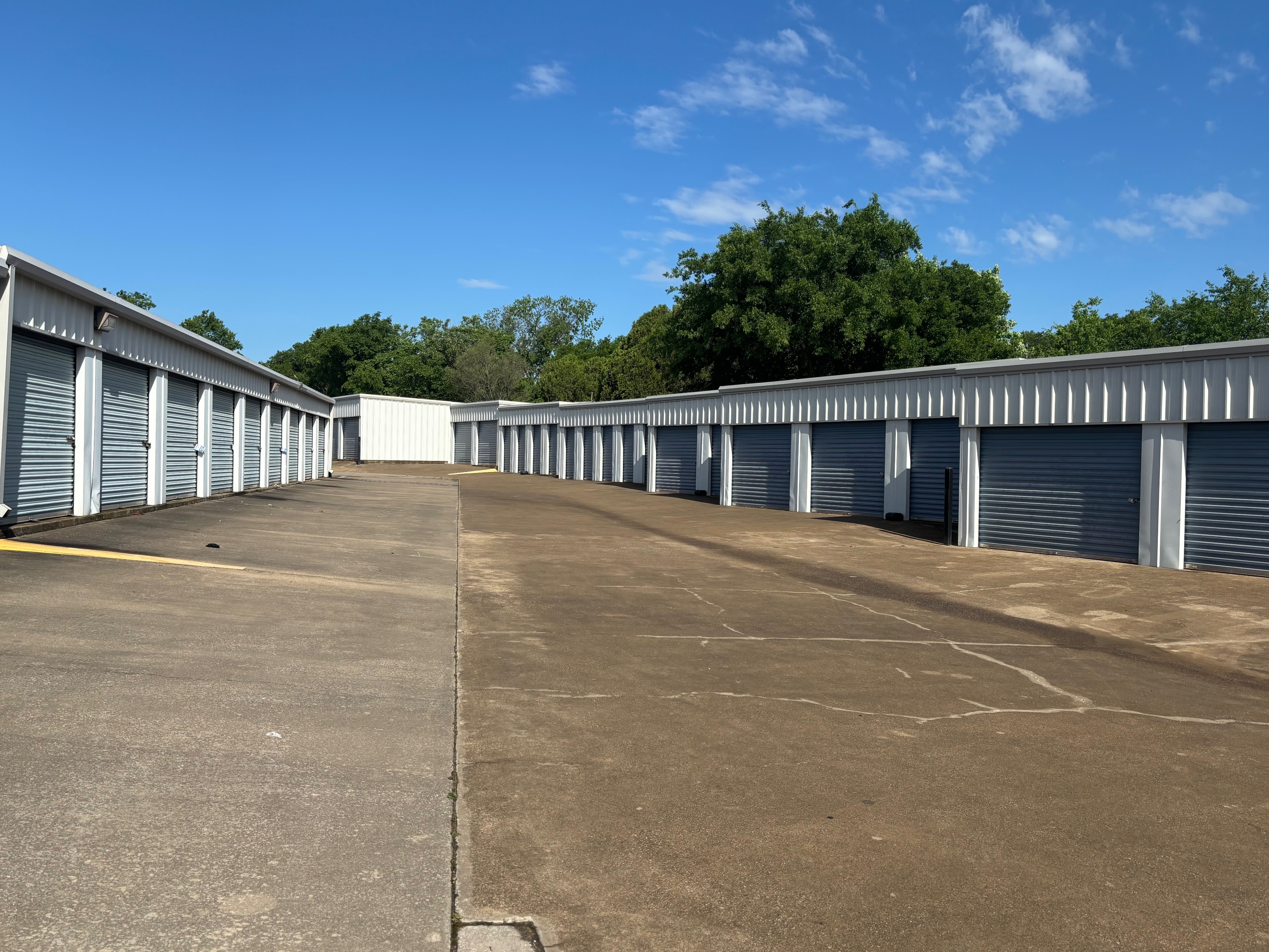Outdoor self-storage units with roll-up doors and wide concrete driveways at Spicewood Super Storage near Oak Leaf, TX, under a clear blue sky.